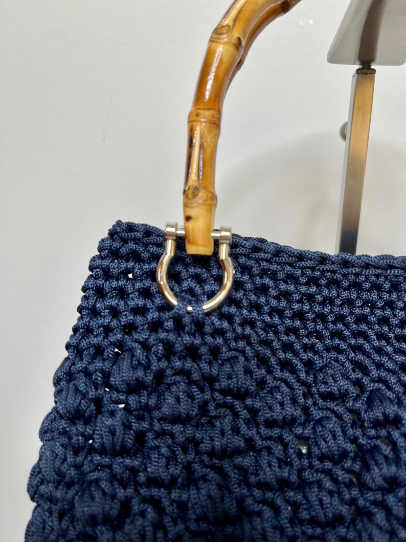May include: A navy blue crocheted tote bag with a bamboo handle and silver hardware.