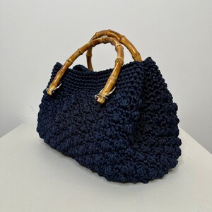 May include: A navy blue crocheted tote bag with bamboo handles. The bag has a textured, woven design.