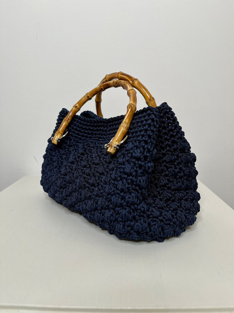 May include: A navy blue crocheted tote bag with bamboo handles. The bag has a textured, woven design.