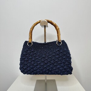 May include: A navy blue crocheted handbag with a bamboo handle. The bag is on a silver stand.