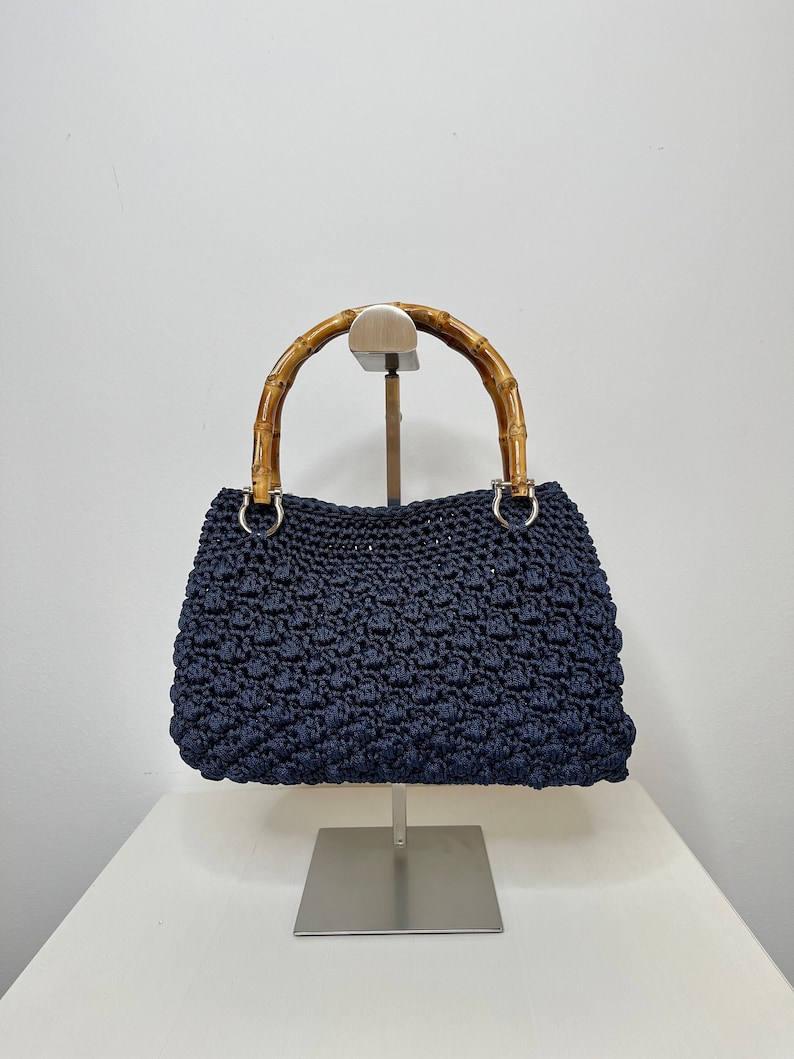 May include: A navy blue crocheted handbag with a bamboo handle. The bag is on a silver stand.
