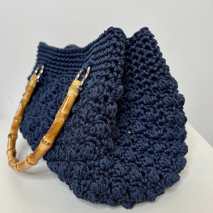 May include: A navy blue crocheted tote bag with bamboo handles. The bag has a textured, woven design.