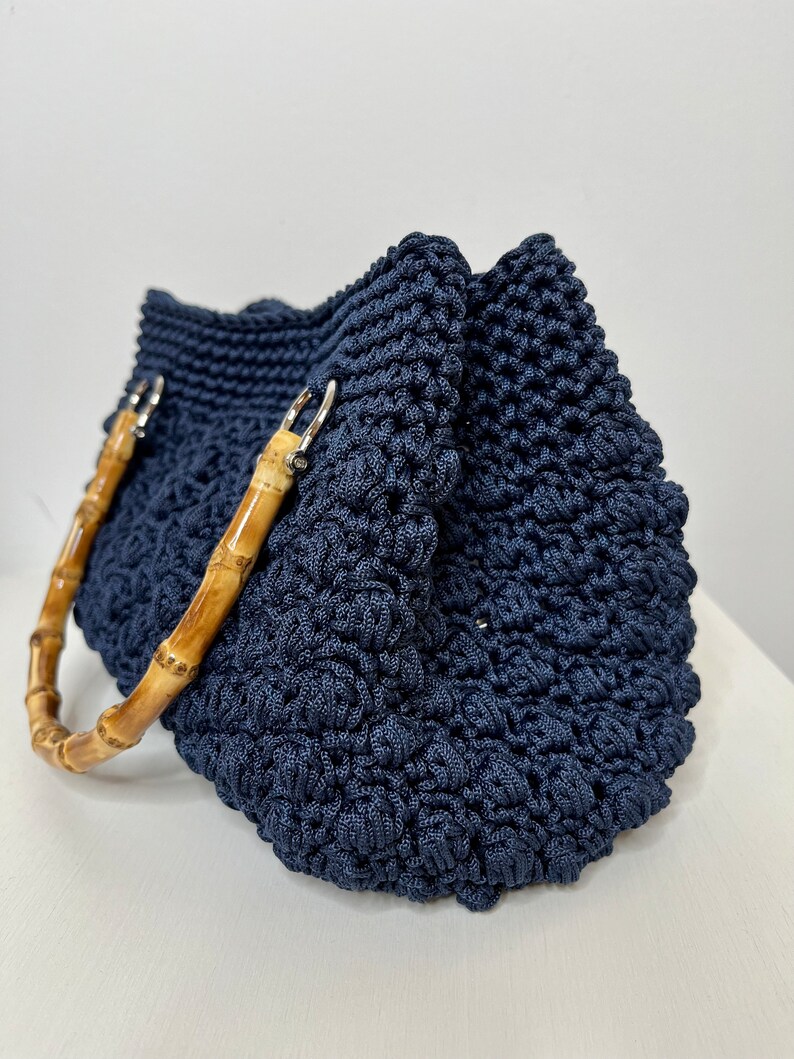 May include: A navy blue crocheted tote bag with bamboo handles. The bag has a textured, woven design.
