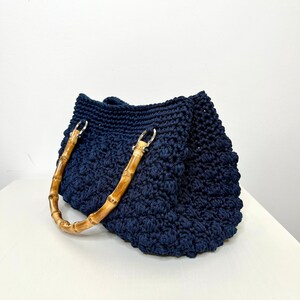 May include: A navy blue crocheted tote bag with bamboo handles.