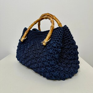May include: A navy blue crocheted handbag with bamboo handles. The bag has a textured, woven design.
