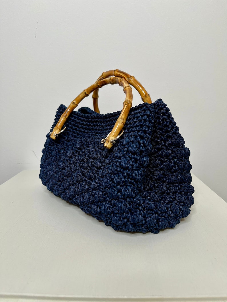 May include: A navy blue crocheted handbag with bamboo handles. The bag has a textured, woven design.