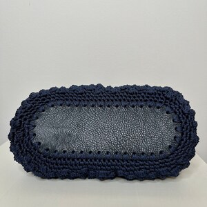 May include: A navy blue crocheted tote bag with a leather base. The bag has a rounded shape and a textured design.