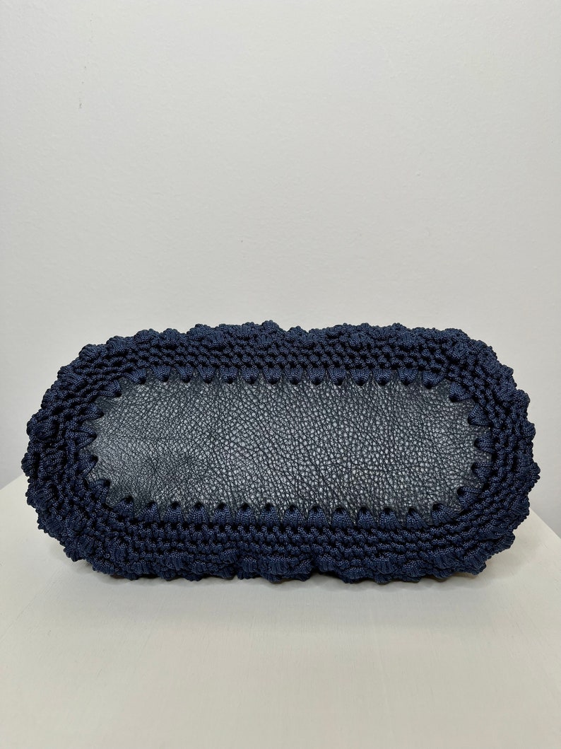 May include: A navy blue crocheted tote bag with a leather base. The bag has a rounded shape and a textured design.