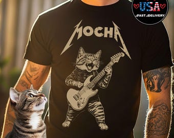 May include: Black t-shirt featuring a cat playing an electric guitar. The word "MOCHA" is above the cat in a stylized font. The cat is brown and tan, and the guitar is beige. The shirt has a "USA Fast Delivery" logo.