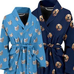 May include: Two bathrobes, one blue and one light blue, with a pattern of dog and cat faces. The robes have a shawl collar and a tie belt.