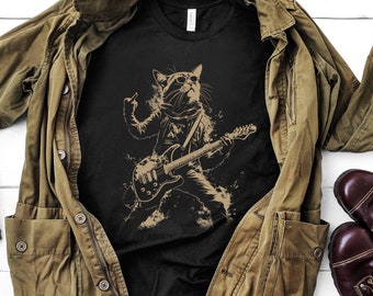 May include: Black t-shirt with a graphic of a cat playing an electric guitar. The cat is wearing a leather jacket and sunglasses. The background is a black and white splatter design.