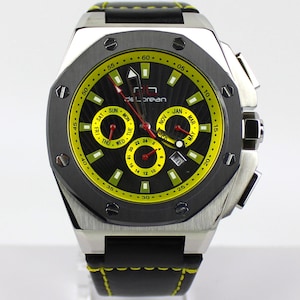 Könnte beinhalten: Eine Edelstahl-De Lorean-Uhr mit schwarzem und gelbem Zifferblatt. Die Uhr hat ein schwarzes Lederarmband mit gelben Nähten. Das Zifferblatt zeigt Tag, Datum und Monat an.