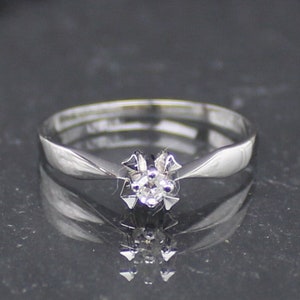 May include: A simple silver band ring with a single, small, round diamond in the centre.