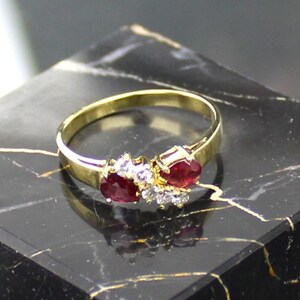 Peut inclure: Une bague en or avec deux pierres précieuses rouges et de petites pierres précieuses blanches serties dans la bande.