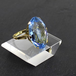 Puede incluir: Un anillo de oro con una gran piedra preciosa ovalada de color azul claro.