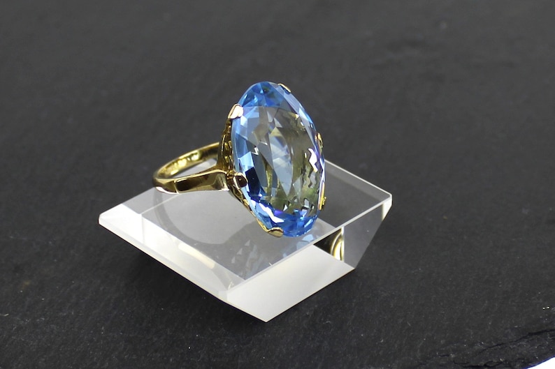 Puede incluir: Un anillo de oro con una gran piedra preciosa ovalada de color azul claro.