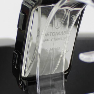 May include: A black digital watch with a rectangular case and a black strap. The back of the watch case features the text ETOMASO, LEGACY TIMELINE, G-30723B, and a shield logo. The watch is mounted on a clear plastic display stand.