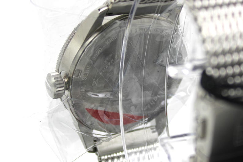 K&ouml;nnte beinhalten: Eine silberne Uhr mit einem Edelstahlband. Das Zifferblatt der Uhr ist mit einer durchsichtigen Plastikabdeckung versehen. Auf der R&uuml;ckseite der Uhr ist der Text "AL SERIES 19920 MADE IN JAPAN" eingraviert.