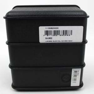 K&ouml;nnte beinhalten: Schwarze Uhrenbox mit einem wei&szlig;en Etikett mit der Aufschrift "111506200000", "7 811382 830483", "XA.9522", "LUM 9522, BLACK DIAL, S/S MESH BAND".