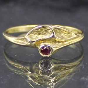 Peut inclure: Une bague en or avec un design texturé organique et une seule pierre précieuse rouge au centre.