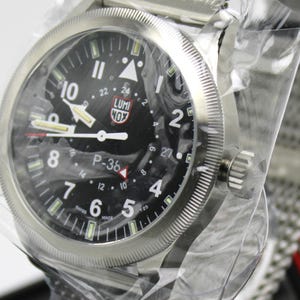 K&ouml;nnte beinhalten: Eine silberne Armbanduhr mit schwarzem Zifferblatt und wei&szlig;en Markierungen. Die Uhr hat ein schwarzes Lederarmband und eine silberne Schlie&szlig;e. Auf dem Zifferblatt der Uhr sind die Worte "LUMI NOX" und "P-36" aufgedruckt.