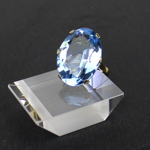 Puede incluir: Un anillo de oro con una gran piedra preciosa ovalada de color azul claro.