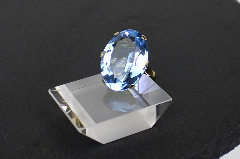 Puede incluir: Un anillo de oro con una gran piedra preciosa ovalada de color azul claro.