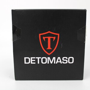 May include: A square black box featuring the white text DETOMASO centered at the bottom. Above the text is a red shield emblem containing a large red letter T. The box has a smooth, matte finish and appears to be a product packaging container.