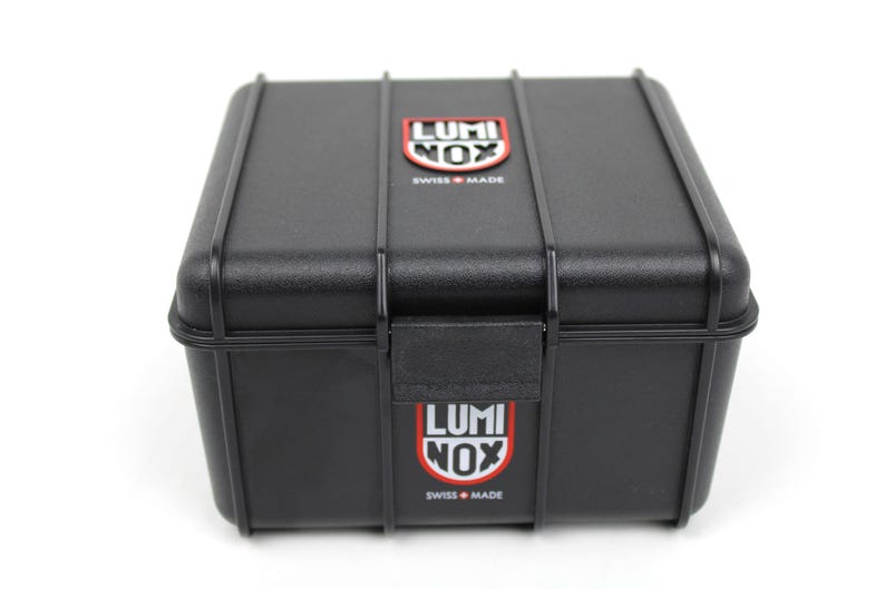 K&ouml;nnte beinhalten: Eine schwarze Plastik-Uhrenbox mit dem Luminox-Logo oben und unten. Das Logo ist rot und wei&szlig; mit dem Text "Luminox" und "Swiss Made".