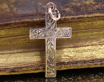 May include: A gold-toned cross pendant with an intricate floral design. The cross is on a brown leather background.