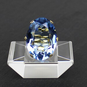 Puede incluir: Un anillo de oro con una piedra preciosa azul. El anillo se muestra en un soporte transparente.