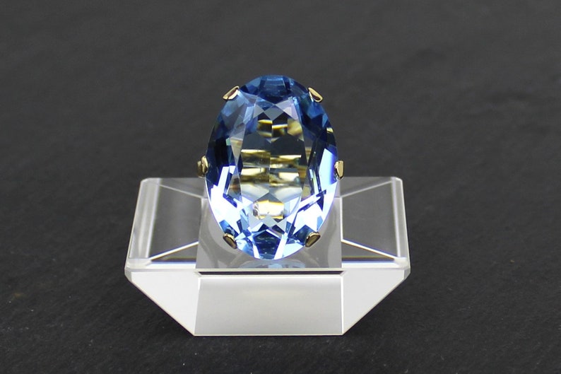 Puede incluir: Un anillo de oro con una piedra preciosa azul. El anillo se muestra en un soporte transparente.