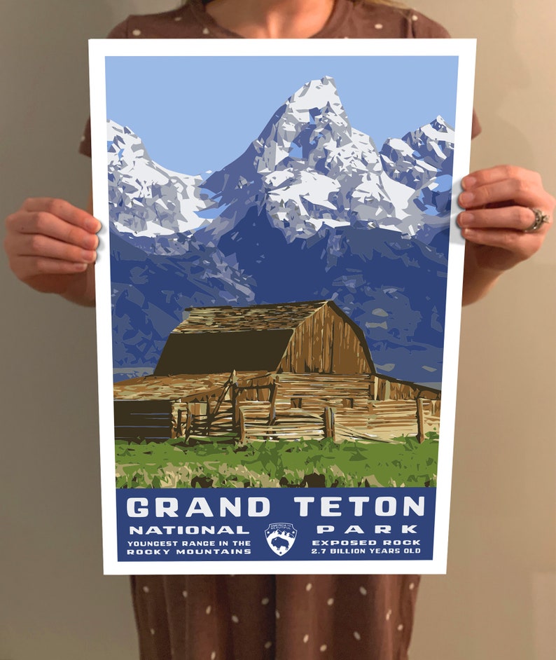 May include: A vintage-style poster featuring a scenic view of the Grand Teton National Park in Wyoming. The poster depicts a rustic wooden barn in the foreground with snow-capped mountains in the background. The text "Grand Teton National Park" is displayed in blue lettering with the park logo and the tagline "Youngest Range in the Rocky Mountains" and "Exposed Rock 2.7 Billion Years Old".