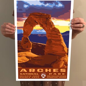 May include: A vintage-style poster featuring a scenic view of Delicate Arch in Arches National Park, Utah. The poster has a sunset sky with orange, yellow, and purple hues. The text reads "Arches National Park" with the park logo and "Delicate Arch, Double Arch, More than 2,000 Natural Sandstone Arches."