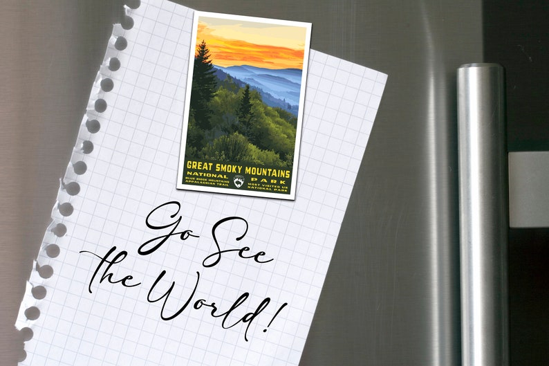 Op de afbeelding: Een wit vel papier met een rasterpatroon en een gescheurde rand. Op het papier staat de tekst "Go See the World!" geschreven in zwarte cursieve letters. Een vintage-achtige ansichtkaart met een zonsondergangsscene van het Great Smoky Mountains National Park is met een magneet aan het papier bevestigd.