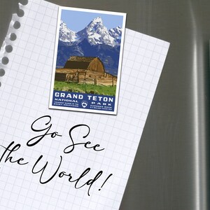 May include: A white notepad with a blue and white Grand Teton National Park postcard attached to it with the text "Go See the World!" written in black cursive.