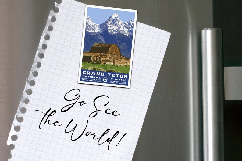 May include: A white notepad with a blue and white Grand Teton National Park postcard attached to it with the text "Go See the World!" written in black cursive.