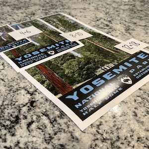 Może przedstawiać: Trzy r&oacute;żne rozmiary plakat&oacute;w Parku Narodowego Yosemite z czarnym tłem i niebieskim tekstem. Tekst brzmi "Yosemite National Park, Yosemite Falls, Half Dome, Założony w październiku 1890". Plakaty przedstawiają panoramiczny widok lasu z wysokimi drzewami.