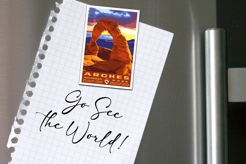 May include: A white notepad with a handwritten message that says "Go See the World!"  A magnet with a picture of Delicate Arch in Arches National Park is attached to the notepad.