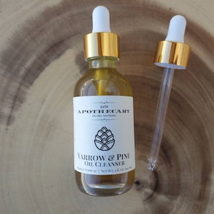 May include: A glass bottle with a gold lid and dropper, filled with a clear liquid. The label reads "12th APOTHECARY Los Olivos, New Mexico YARROW & PINE OIL CLEANSER HERBAL TOPICAL | NET WT. 1 FL. OZ. (30 ml)"
