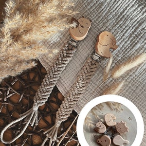 Könnte beinhalten: Zwei Holz-Beißringe mit einer geflochtenen Schnur. Die Beißringe sind in Form eines Fuchses und eines Elefanten. Eine Nahaufnahme der Beißringe zeigt verschiedene Tierformen.