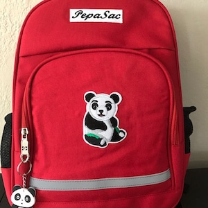 May include: Red backpack with a panda bear design and the text "Pepa Sac" on the front. The backpack has a reflective strip and a zipped pocket.