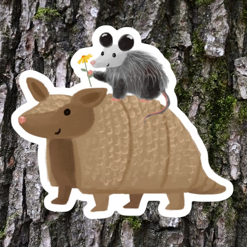 May include: A brown armadillo with a gray opossum riding on its back. The opossum is holding a yellow flower.