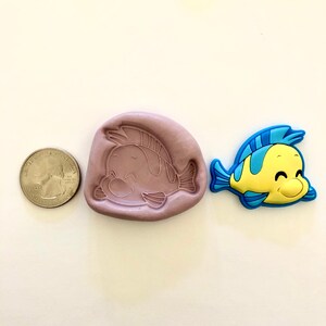 Pu&ograve; includere: Uno stampo in silicone per realizzare un piccolo pesce giallo con pinne blu. Lo stampo &egrave; viola e ha un'impressione dettagliata del pesce. Un piccolo pesce giallo con pinne blu &egrave; mostrato accanto allo stampo.