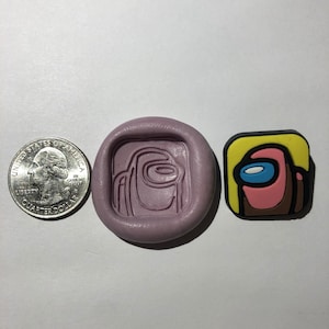 May include: A purple silicone mold for making a pink and brown Among Us character. The mold is about the size of a US quarter.