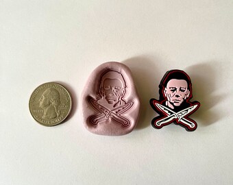 May include: A pink silicone mold of a character with a knife, next to a black and white character with a knife. The character is a man with a white face and black hair. The mold is about the size of a US quarter.