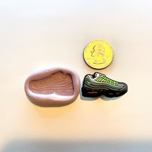 May include: A silicone mold for making a miniature replica of a black and green sneaker. The mold is next to a quarter for size comparison.