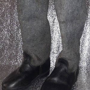 Puede incluir: Un par de botas de cuero negro con empeines de fieltro gris. Las botas tienen una punta redonda y un tacón bajo.