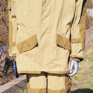 May include: A tan and brown camouflage military uniform with a hood. The uniform is made of a thick, durable fabric and has a zipper closure. The uniform is designed for cold weather and has a variety of pockets for carrying gear.