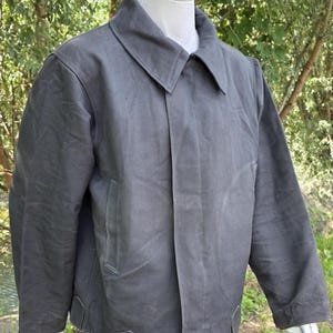 K&ouml;nnte beinhalten: Anthrazitfarbene Jacke mit breitem Kragen und zwei Vordertaschen. Die Jacke hat einen Knopfverschluss und einen geraden Saum. Die langen &Auml;rmel haben einfache Manschetten. Die Jacke ist aus robustem Material gefertigt.